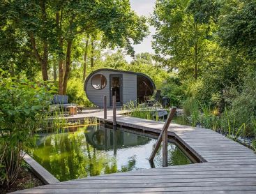 A swimming pond in a small garden with a sauna house surrounded by trees